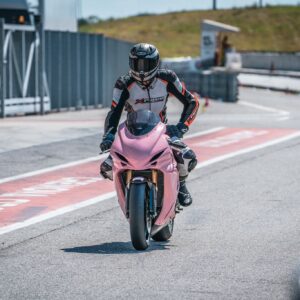 Pilota in tuta da corsa su una moto sportiva rosa in pista, pronto per la gara.