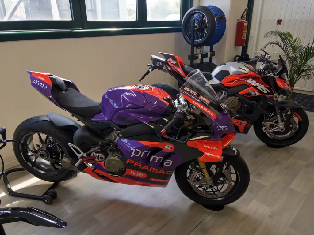 Moto Ducati Pramac in livrea viola e rossa e Moto Ducati V4 in un ambiente interno.